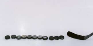 A row of hockey pucks and a stick on an ice rink, perfect for sports content.