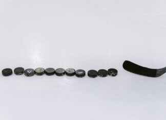 A row of hockey pucks and a stick on an ice rink, perfect for sports content.