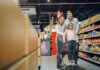 Family enjoying a shopping trip in a supermarket, with a child in a cart and parents smiling.