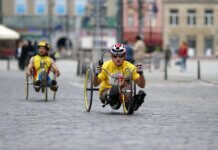Two athletes in handcycles compete on a city street, showcasing strength and speed.
