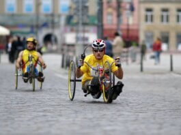 Two athletes in handcycles compete on a city street, showcasing strength and speed.