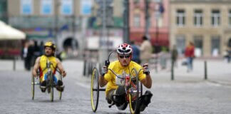 Two athletes in handcycles compete on a city street, showcasing strength and speed.