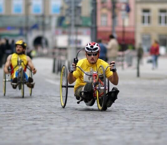 Two athletes in handcycles compete on a city street, showcasing strength and speed.