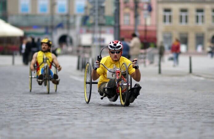 Two athletes in handcycles compete on a city street, showcasing strength and speed.