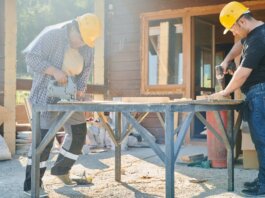 Two construction workers using power tools on a sunny day.