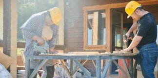 Two construction workers using power tools on a sunny day.