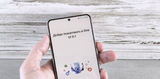 A close-up of a hand holding a smartphone displaying the One UI 6.1 welcome screen indoors.