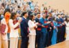 A diverse group of graduates celebrate their achievement in a lively indoor ceremony, showcasing excitement and joy.
