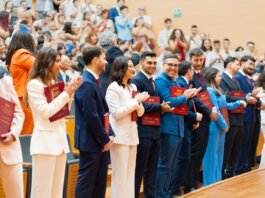 A diverse group of graduates celebrate their achievement in a lively indoor ceremony, showcasing excitement and joy.