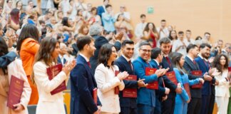 A diverse group of graduates celebrate their achievement in a lively indoor ceremony, showcasing excitement and joy.