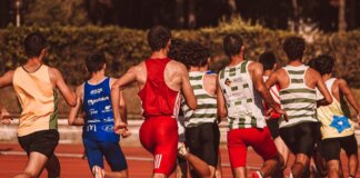 A group of male athletes competing in a track and field event outdoors under a sunny sky.