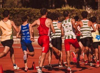 A group of male athletes competing in a track and field event outdoors under a sunny sky.