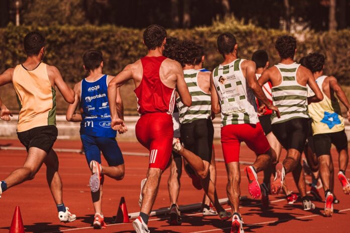 A group of male athletes competing in a track and field event outdoors under a sunny sky.