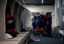 A hockey team in a locker room huddles for motivation, symbolizing teamwork and sportsmanship.