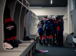 A hockey team in a locker room huddles for motivation, symbolizing teamwork and sportsmanship.
