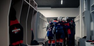 A hockey team in a locker room huddles for motivation, symbolizing teamwork and sportsmanship.