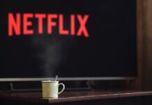 Консерваторы требуют отменить повышение «налога на Netflix» до 15% A steaming mug on a table in front of a TV displaying Netflix, creating a cozy indoor atmosphere.
