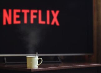 Консерваторы требуют отменить повышение «налога на Netflix» до 15% A steaming mug on a table in front of a TV displaying Netflix, creating a cozy indoor atmosphere.