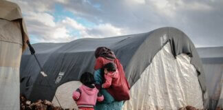 A woman and children walk near tents in a refugee camp in Idlib, showcasing resilience amidst adversity.