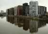 Captivating view of modern high-rise buildings reflecting in a calm river under cloudy skies.