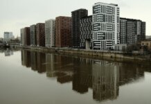 Captivating view of modern high-rise buildings reflecting in a calm river under cloudy skies.