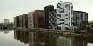 Captivating view of modern high-rise buildings reflecting in a calm river under cloudy skies.
