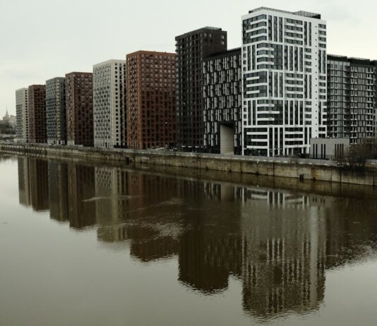 Captivating view of modern high-rise buildings reflecting in a calm river under cloudy skies.