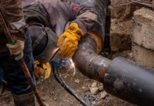 Close-up of a skilled worker welding a steel pipe outdoors at a construction site.
