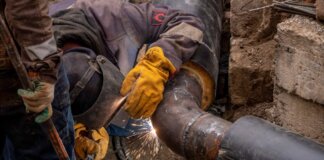 Close-up of a skilled worker welding a steel pipe outdoors at a construction site.