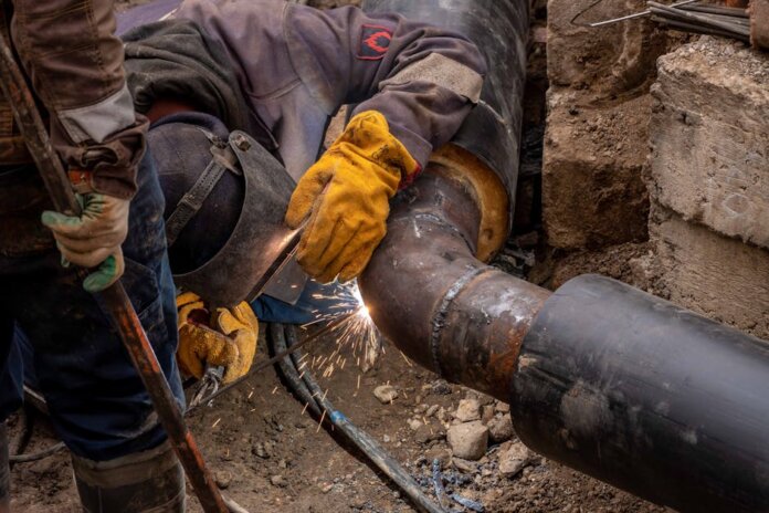 Close-up of a skilled worker welding a steel pipe outdoors at a construction site. Close-up of a skilled worker welding a steel pipe outdoors at a construction site.