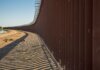 Long view of a steel border wall under clear skies, emphasizing solitude and division.