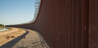 Long view of a steel border wall under clear skies, emphasizing solitude and division.