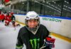 Smiling young ice hockey player posing with gear on an indoor rink.