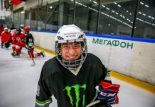 Smiling young ice hockey player posing with gear on an indoor rink.