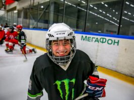 Smiling young ice hockey player posing with gear on an indoor rink.