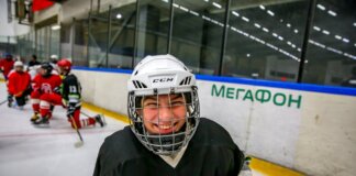 Smiling young ice hockey player posing with gear on an indoor rink.