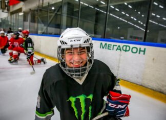 Smiling young ice hockey player posing with gear on an indoor rink.