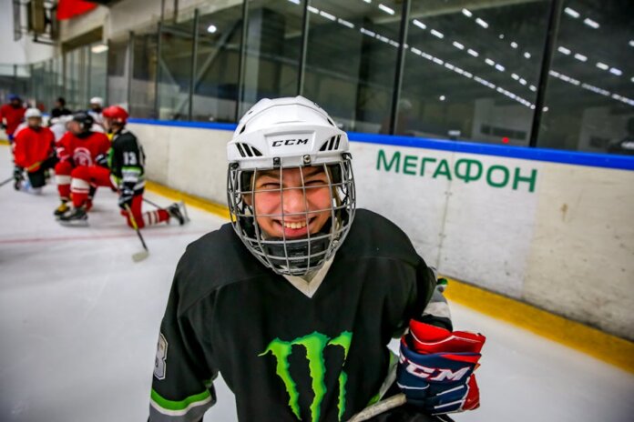 Smiling young ice hockey player posing with gear on an indoor rink.
