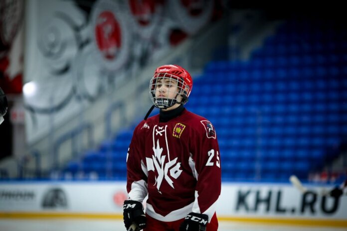 Teen ice hockey player in full gear on an indoor rink, ready for action.