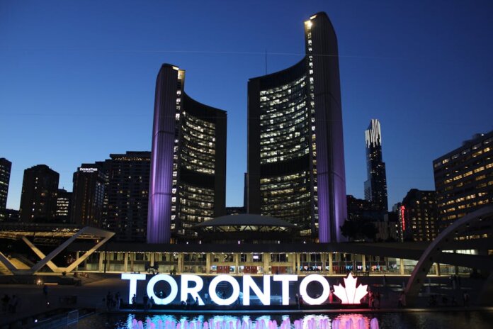 Toronto City Hall stands illuminated against the night sky, showcasing vibrant city lights and iconic architecture.