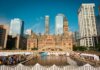 Toronto's historic Old City Hall and Nathan Phillips Square with reflecting pool under blue sky.