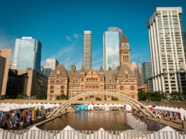 Toronto's historic Old City Hall and Nathan Phillips Square with reflecting pool under blue sky.