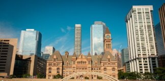Toronto's historic Old City Hall and Nathan Phillips Square with reflecting pool under blue sky.