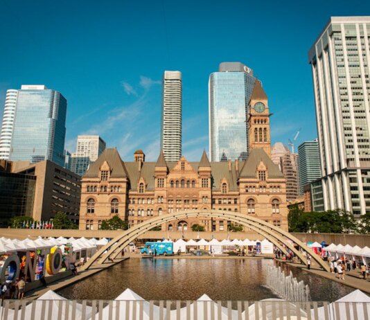 Toronto's historic Old City Hall and Nathan Phillips Square with reflecting pool under blue sky.