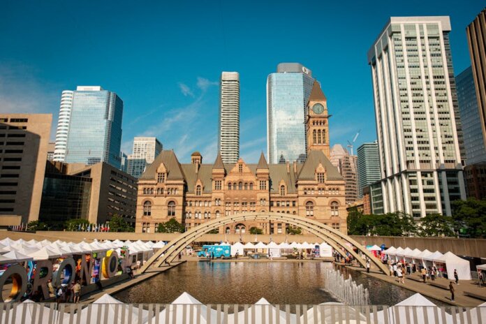 Toronto's historic Old City Hall and Nathan Phillips Square with reflecting pool under blue sky.