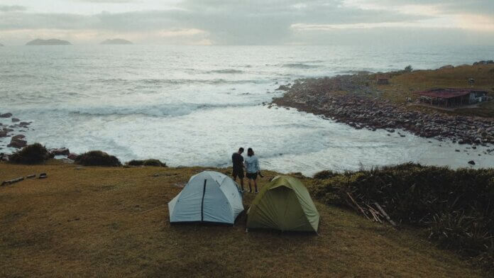 Two tents and a couple enjoying a scenic coastal view in Palhoça, Brazil. Two tents and a couple enjoying a scenic coastal view in Palhoça, Brazil.