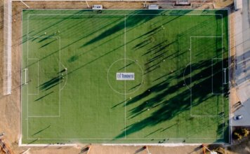 Чемпионат мира по футболу в Торонто вдохновляет новое поколение игроков Aerial view of soccer field with anonymous sportspeople and shades against roadway on sunny day