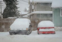 Two snow-covered cars parked on a quiet winter street in Surrey, BC, Canada.