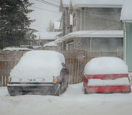 Two snow-covered cars parked on a quiet winter street in Surrey, BC, Canada.