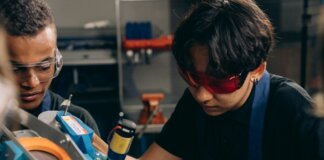 Two young engineers concentrating on precision work in a technical workshop, wearing safety goggles.